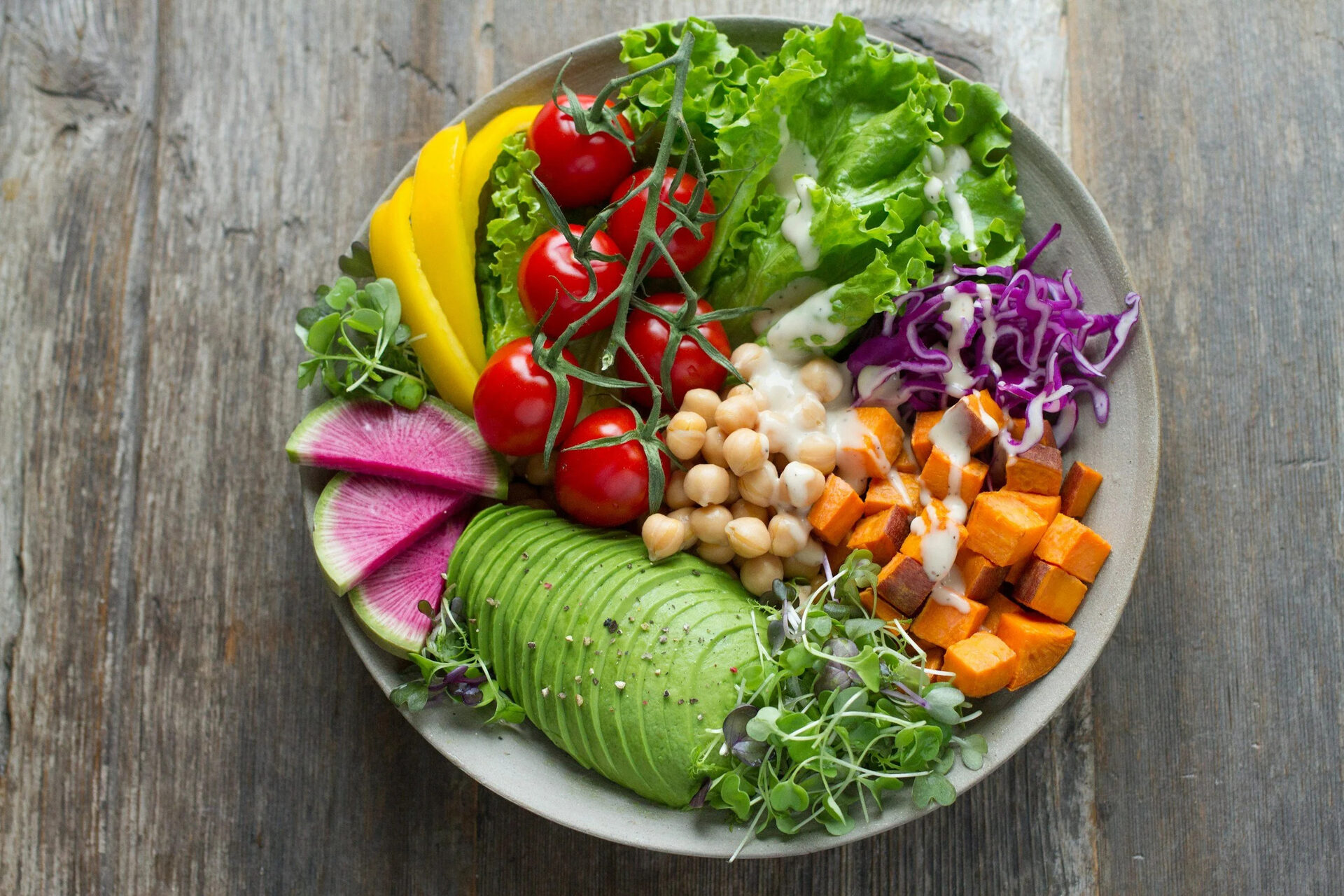 A bowl of fresh vegetables, avocado and chickpeas on a wooden table